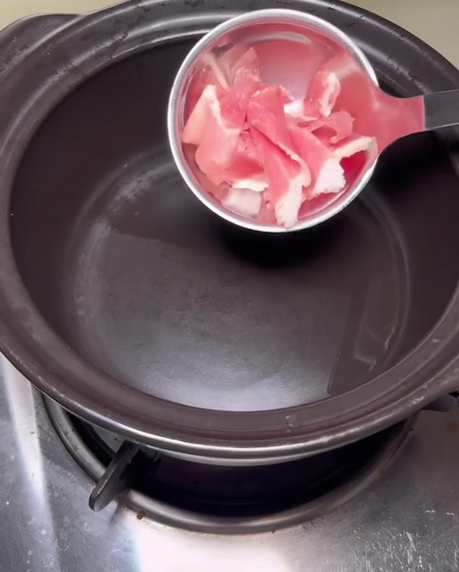 Slices of raw pork belly sizzling in a hot, empty black stone pot.