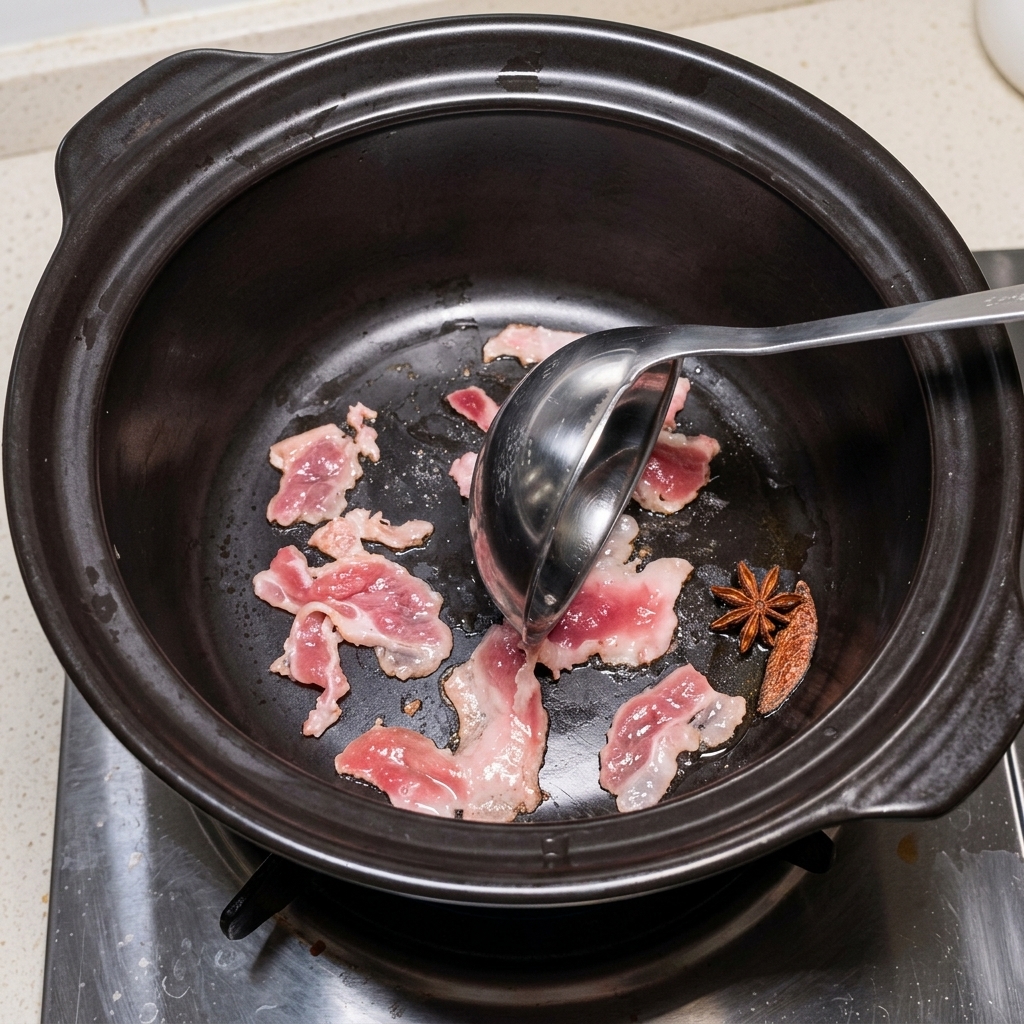 Pork belly slices sizzling in a dark stone pot, being moved with a ladle.