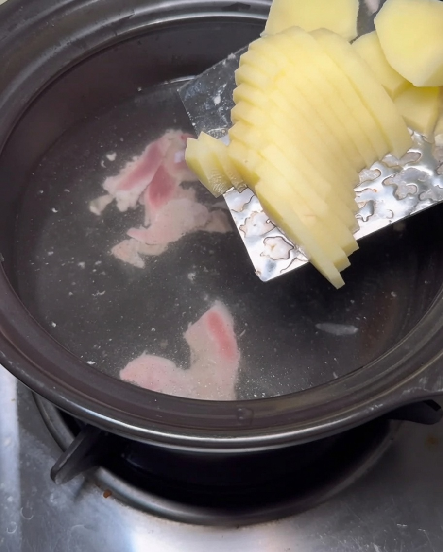 Thick potato slices being slid from a metal blade into a pot of simmering water.