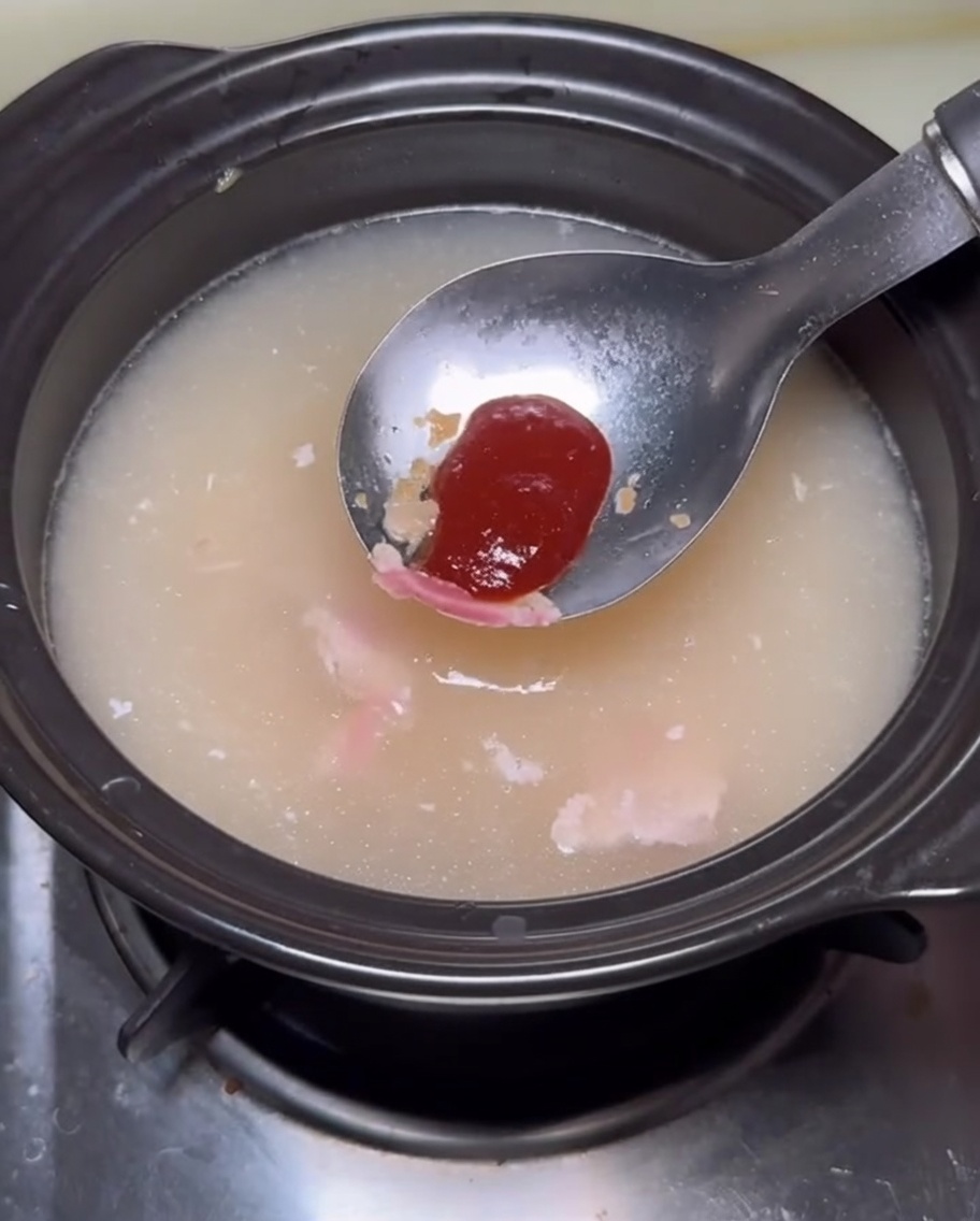 A spoonful of reddish sauce being added into the pot of broth.