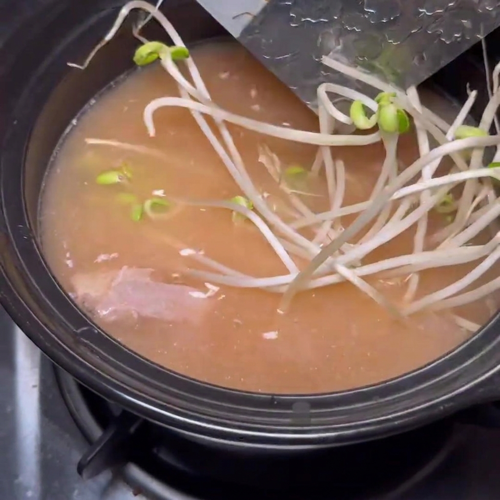 Sliced shiitake mushrooms being added to the bubbling soybean paste stew in a stone pot.
