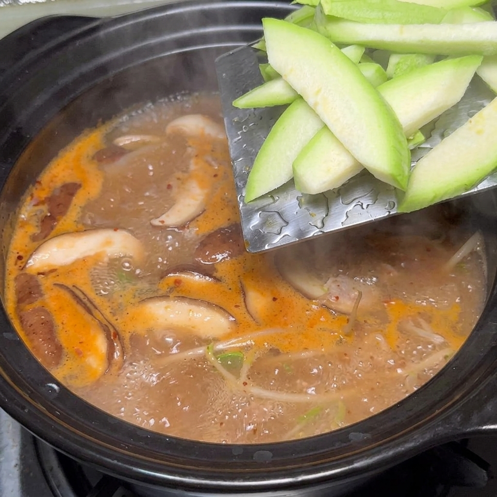 Zucchini slices being added to the simmering pot of soybean paste stew.