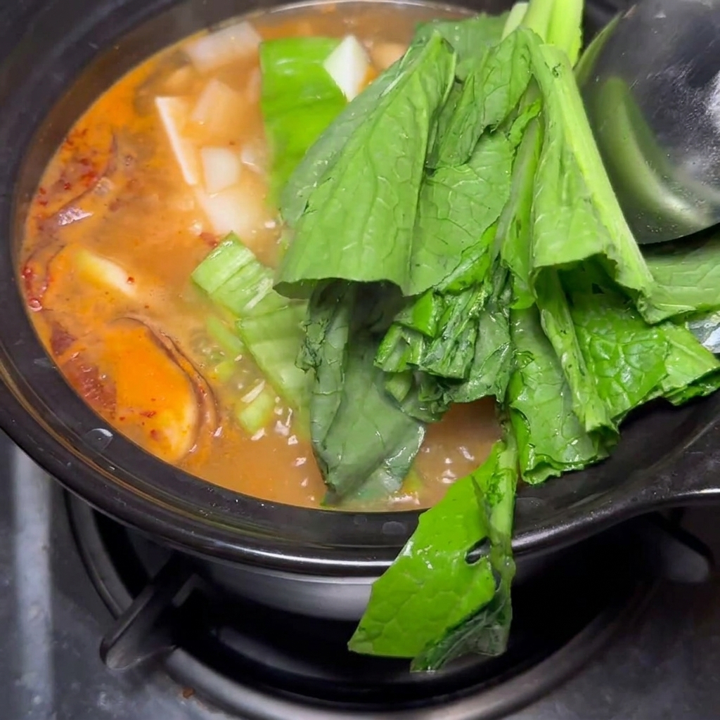Fresh baby bok choy and onion chunks being added to the finished soybean paste stew.
