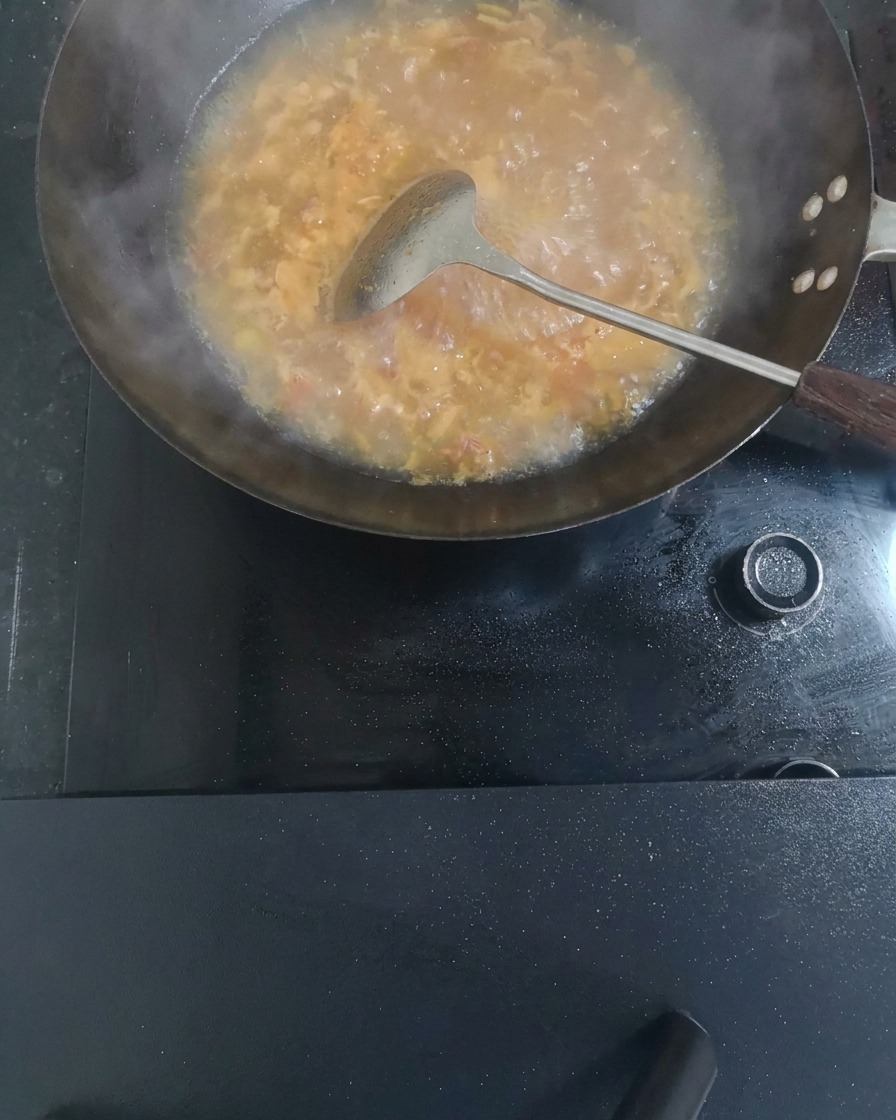 Salt, fresh ginger slices, and light soy sauce being stirred into the boiling tomato soup.