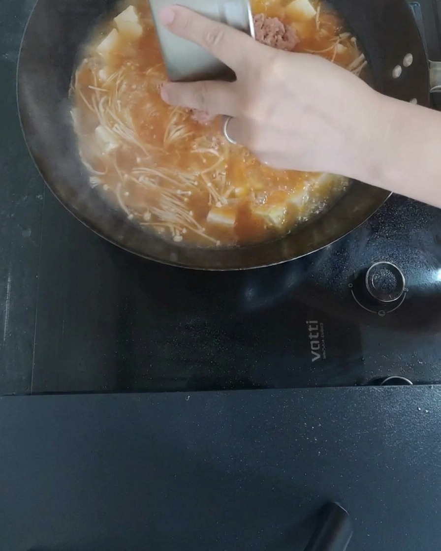 Minced meat being stirred into the boiling soup, breaking apart into small pieces.