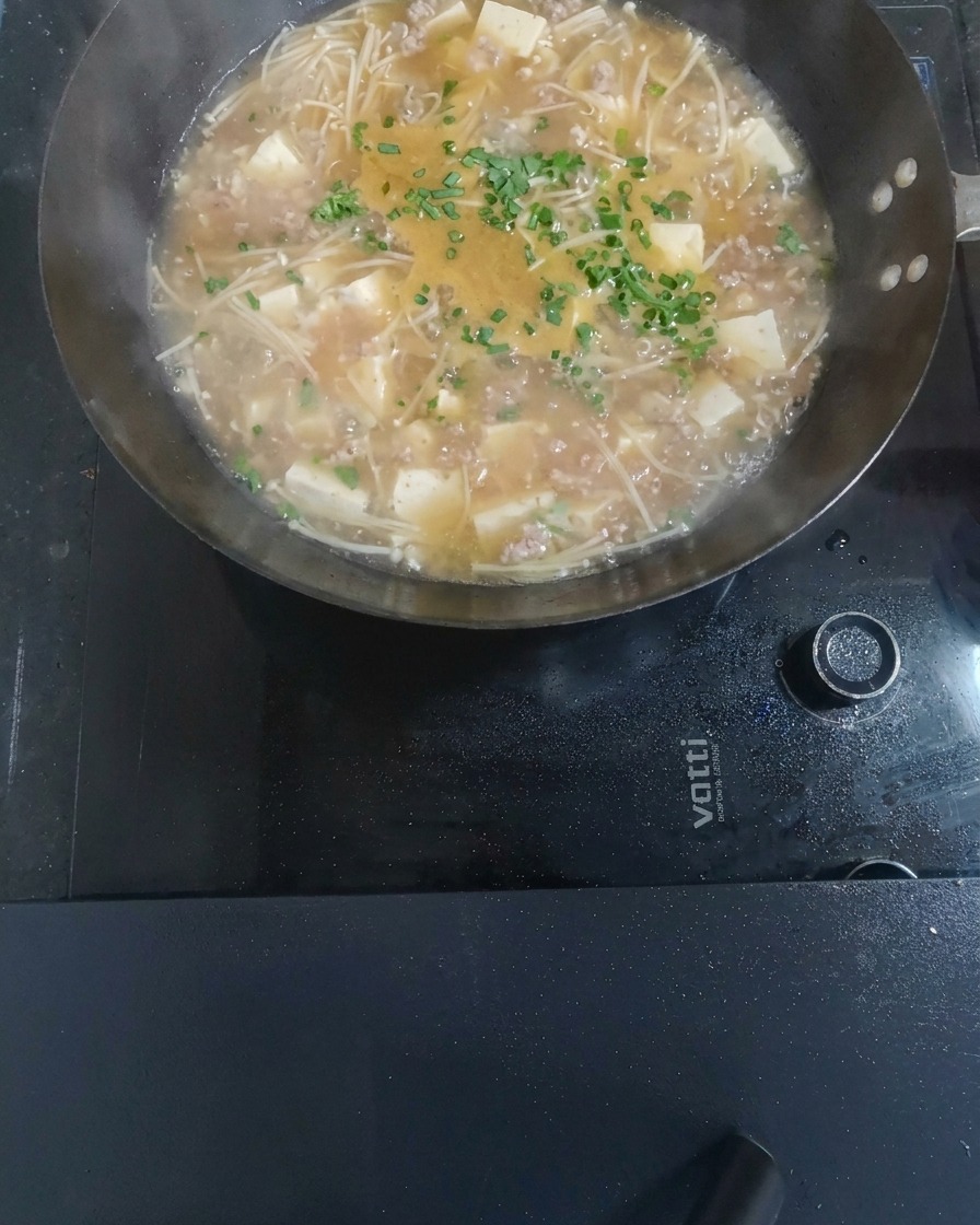 Finished sweet and sour minced meat and tofu soup garnished with chopped green onions.