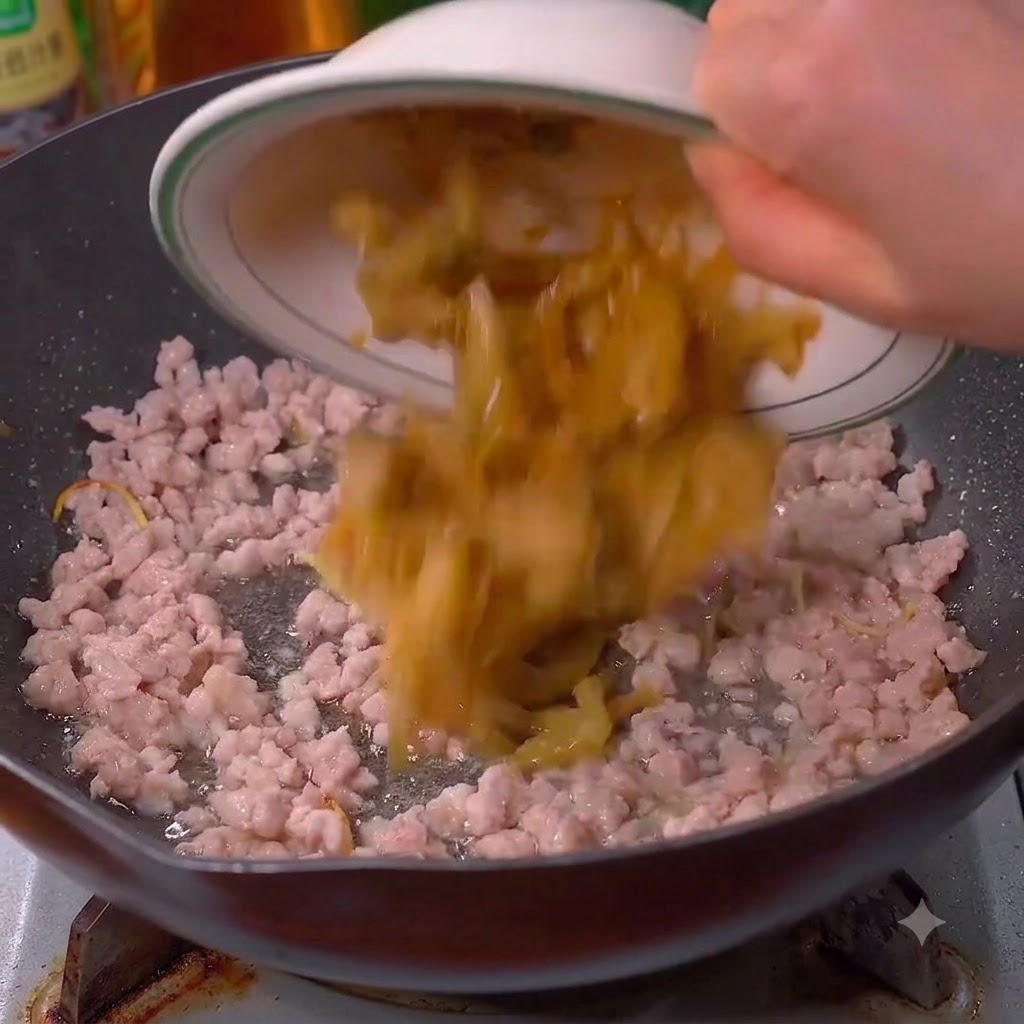 Pickled mustard greens being poured into the wok with pork.