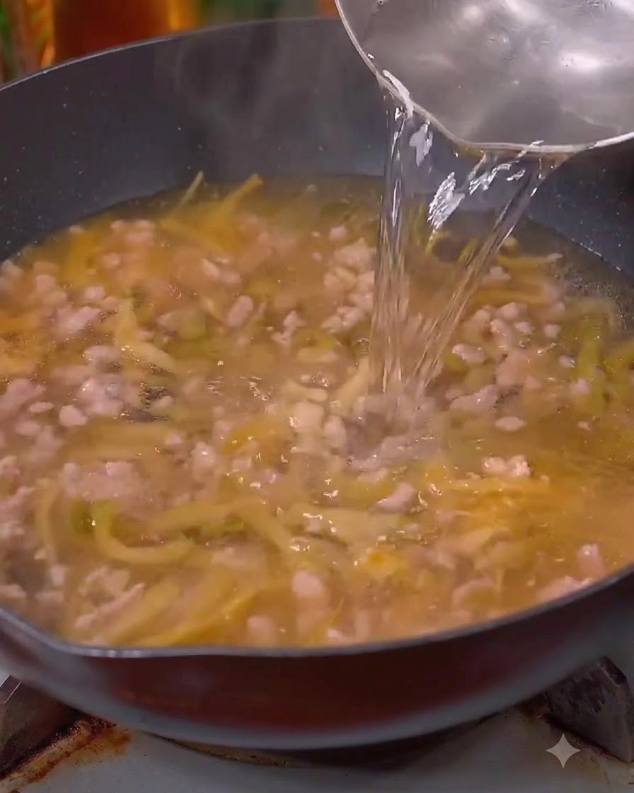 Water being poured into the wok over the meat and greens.