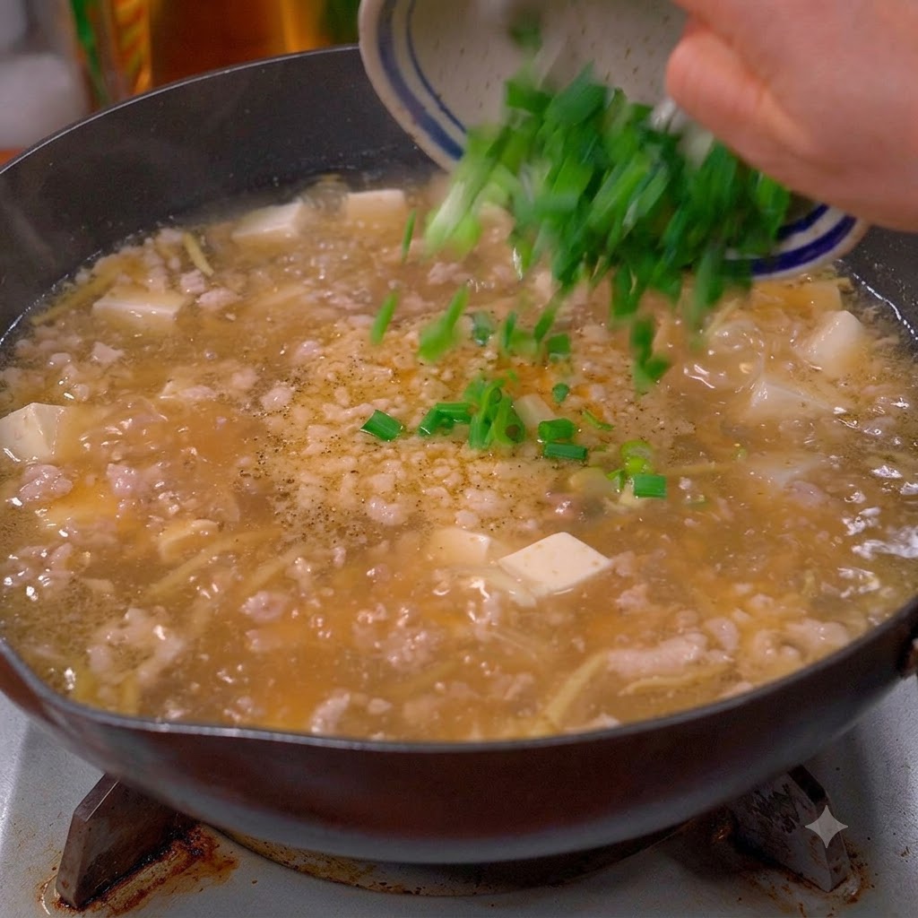 Chopped green scallions and cilantro being tipped from a bowl into a bubbling pot of soup.