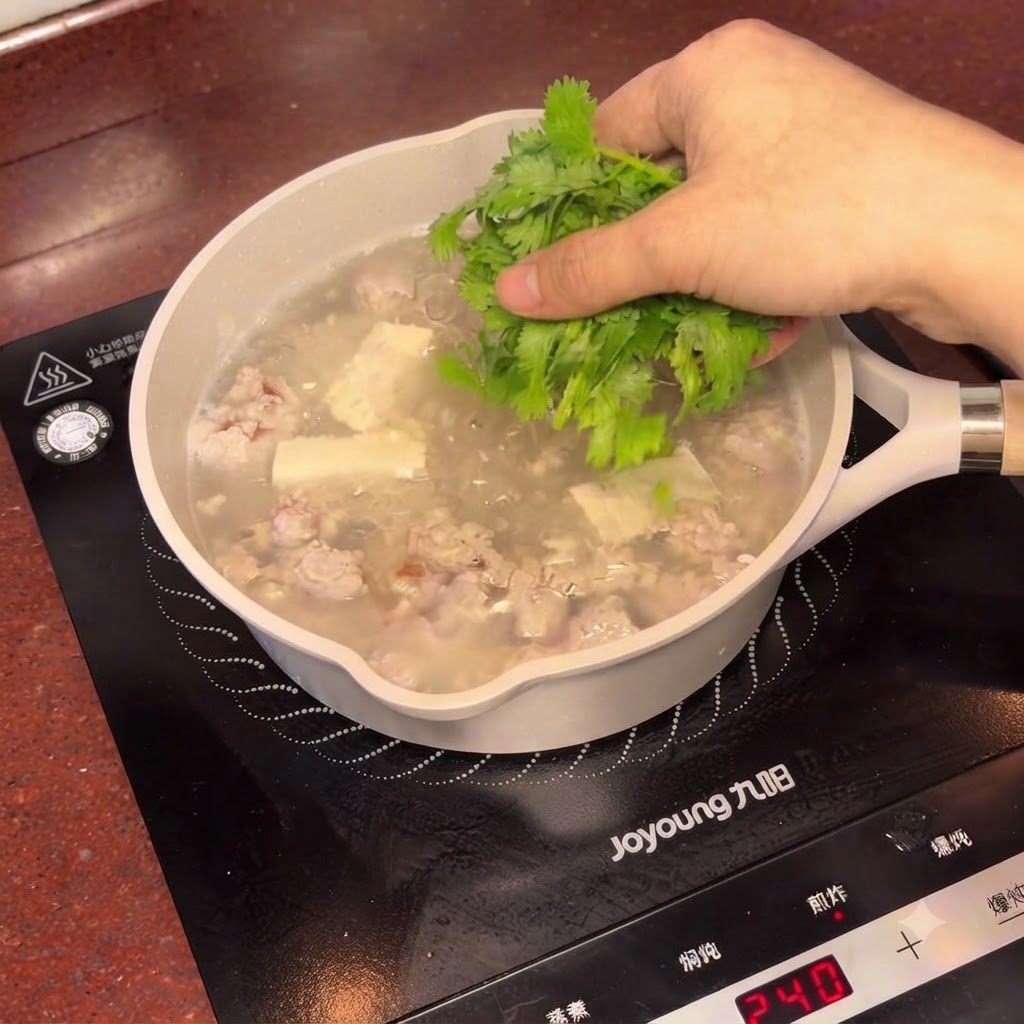 Fresh chopped coriander being sprinkled over the steaming pot of salted plum tofu soup.