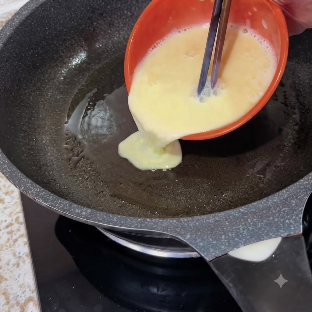 An orange bowl pouring liquid beaten eggs with chopsticks into a hot frying pan.