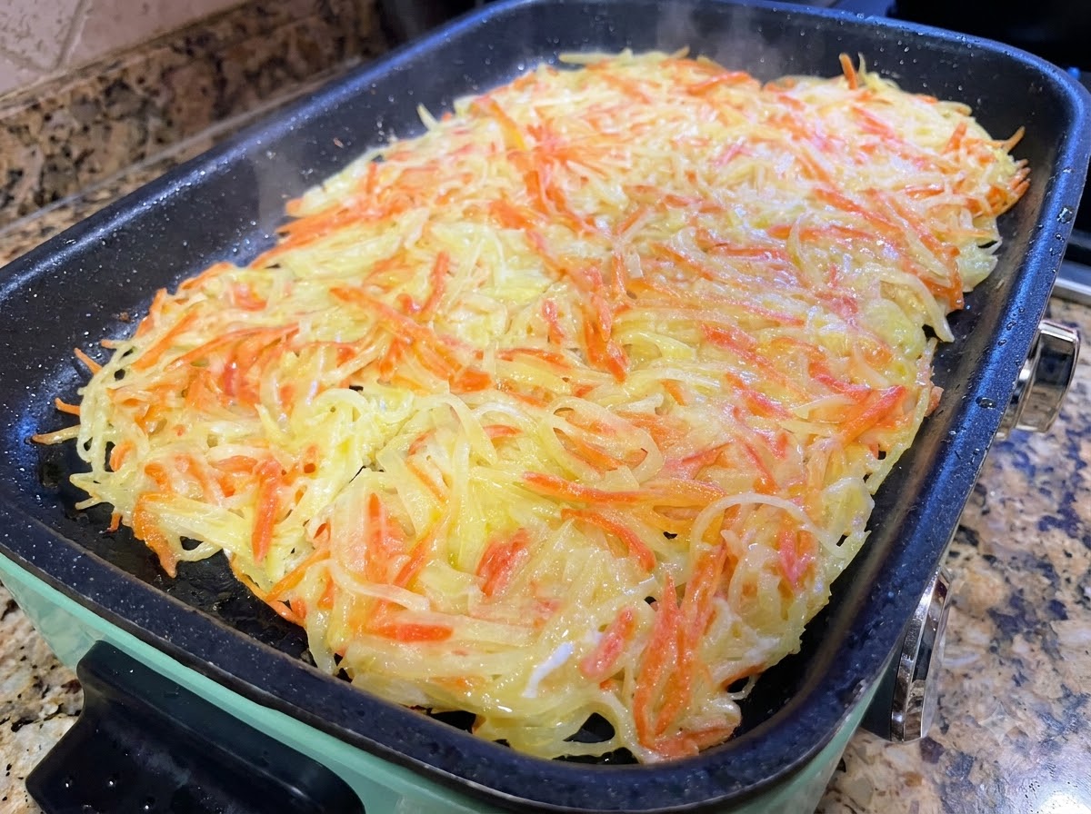 A large potato pancake being sliced into smaller portions with cooking spatulas in a pan.