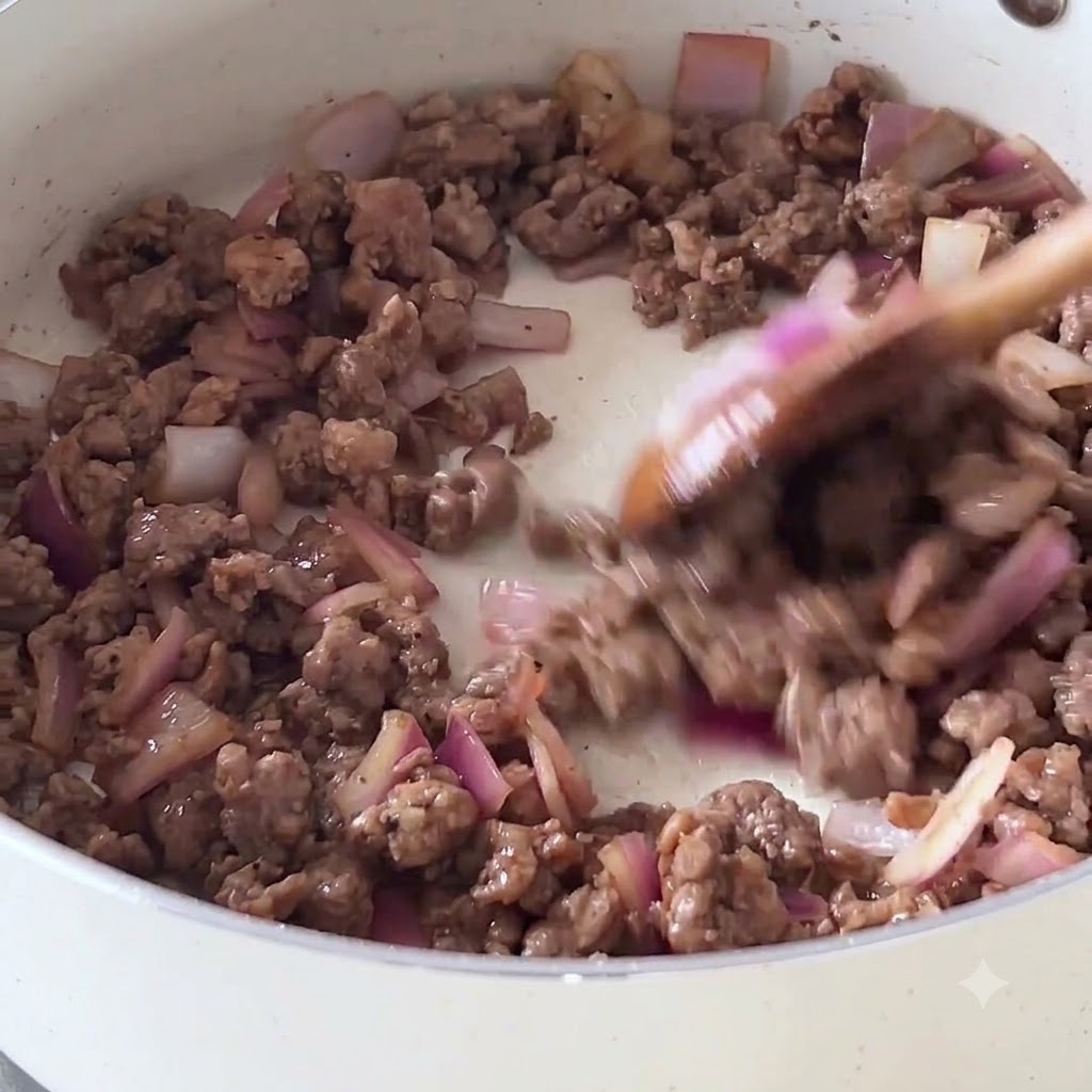 Stir-frying minced beef and chopped purple onions in a white non-stick pan using a wooden spoon.