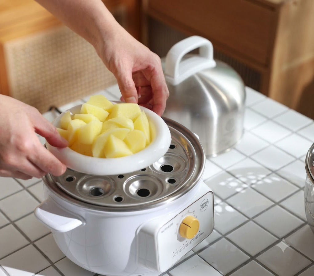 A white dish filled with potato chunks being placed into a steamer pot to cook until tender.
