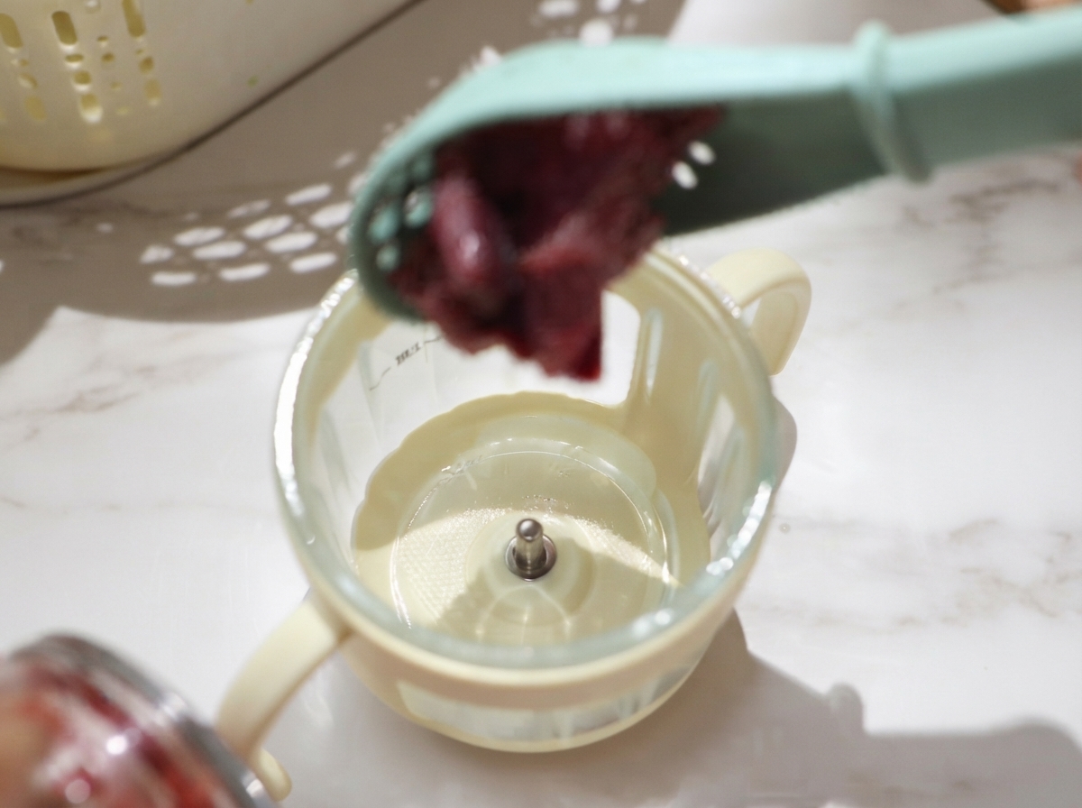 Drained pieces of raw beef being spooned into a small food processor cup for blending.