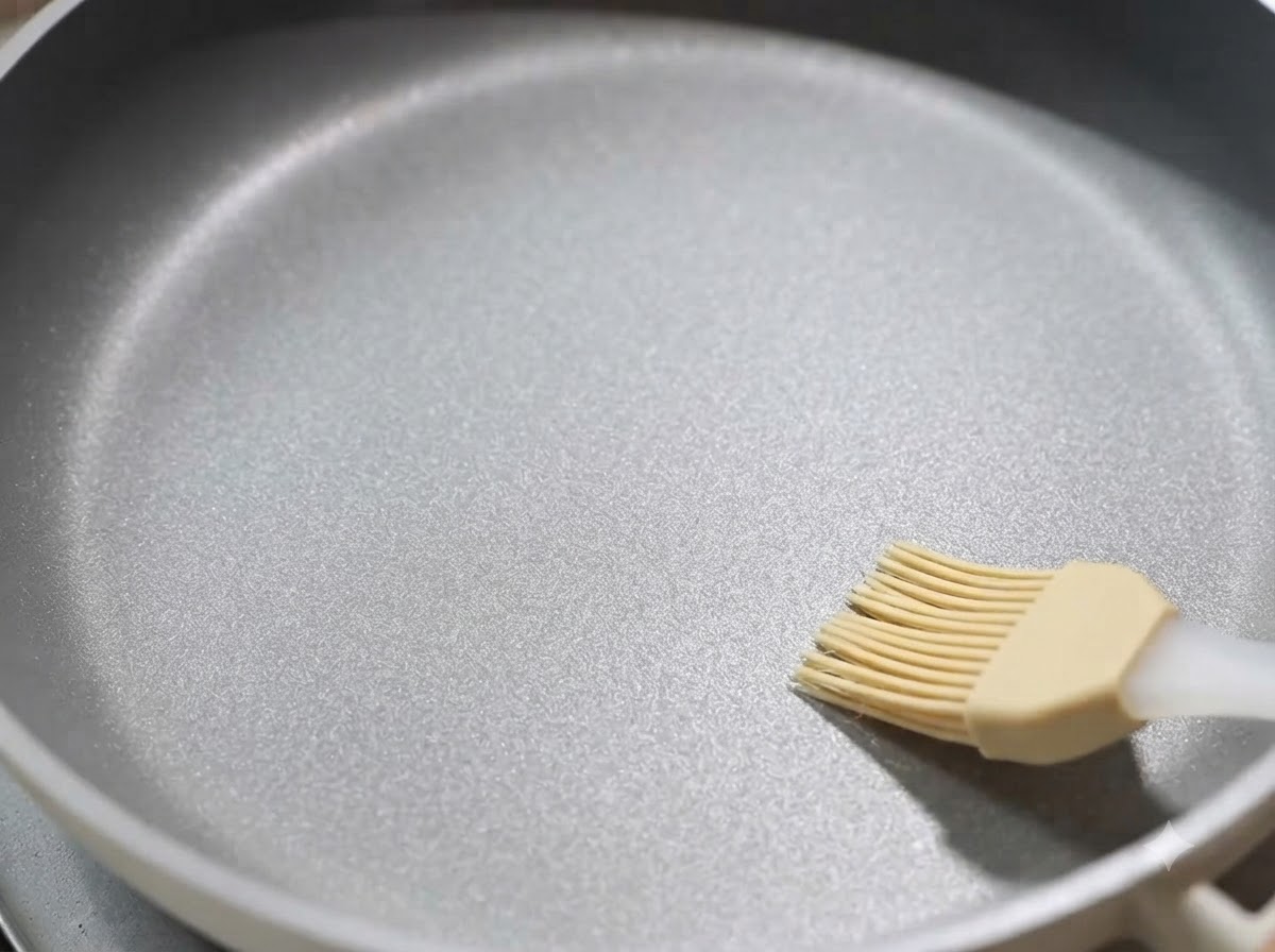 A non-stick frying pan being brushed with a thin layer of cooking oil.