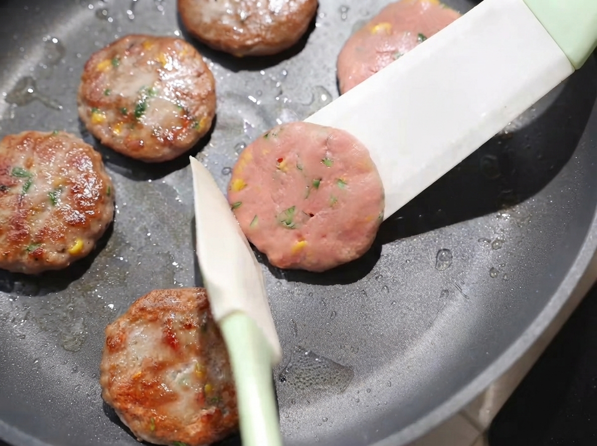 Patties being flipped over in the pan using a spatula, showing golden-brown surfaces being cooked on low heat.