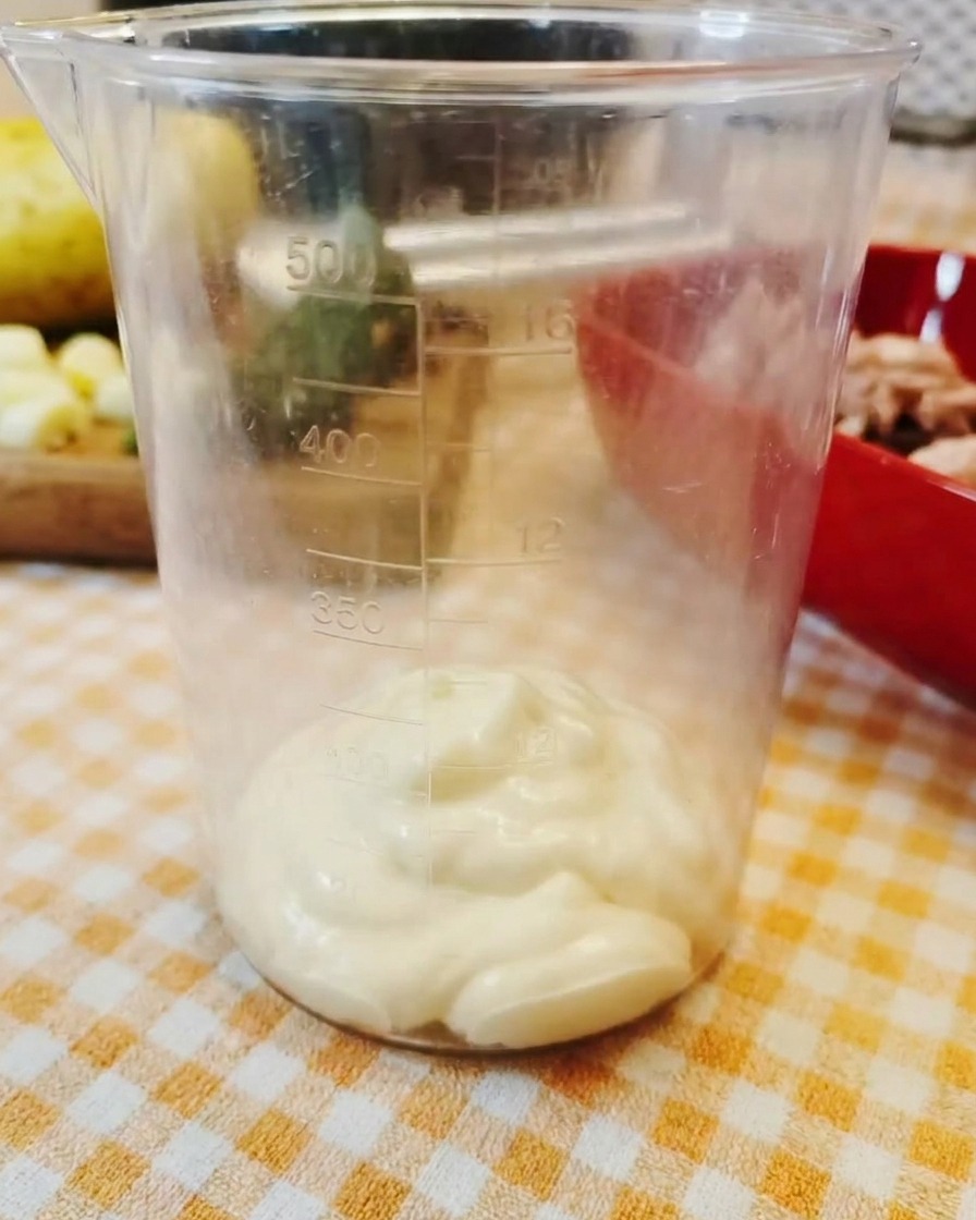 A dollop of thick mayonnaise resting at the bottom of a clear plastic measuring cup.