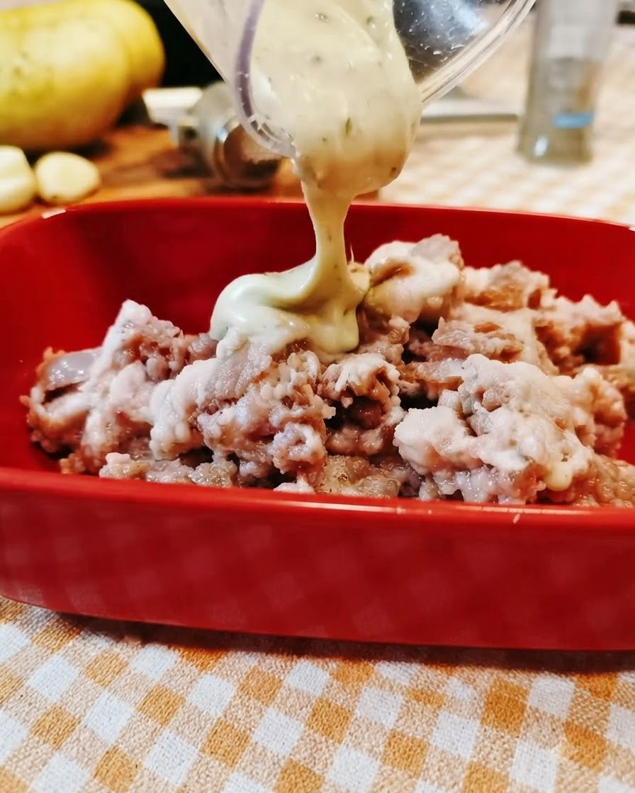 Sauce being poured from a clear container into a red bowl filled with seasoned minced beef.