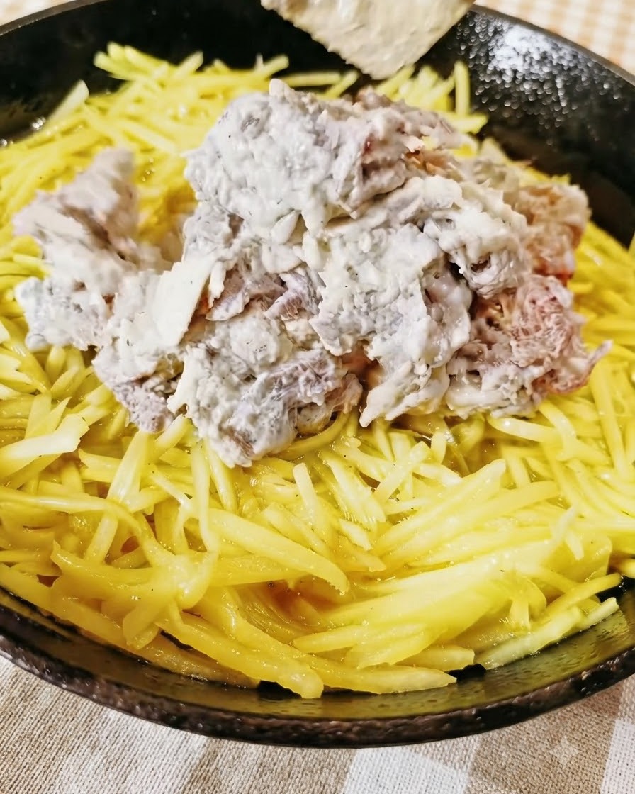 Seasoned minced beef piled on top of a yellow layer of shredded potatoes inside a skillet.