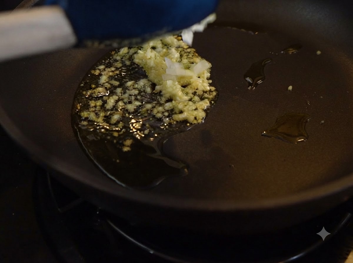 Minced garlic and onions frying in oil inside a dark pan.