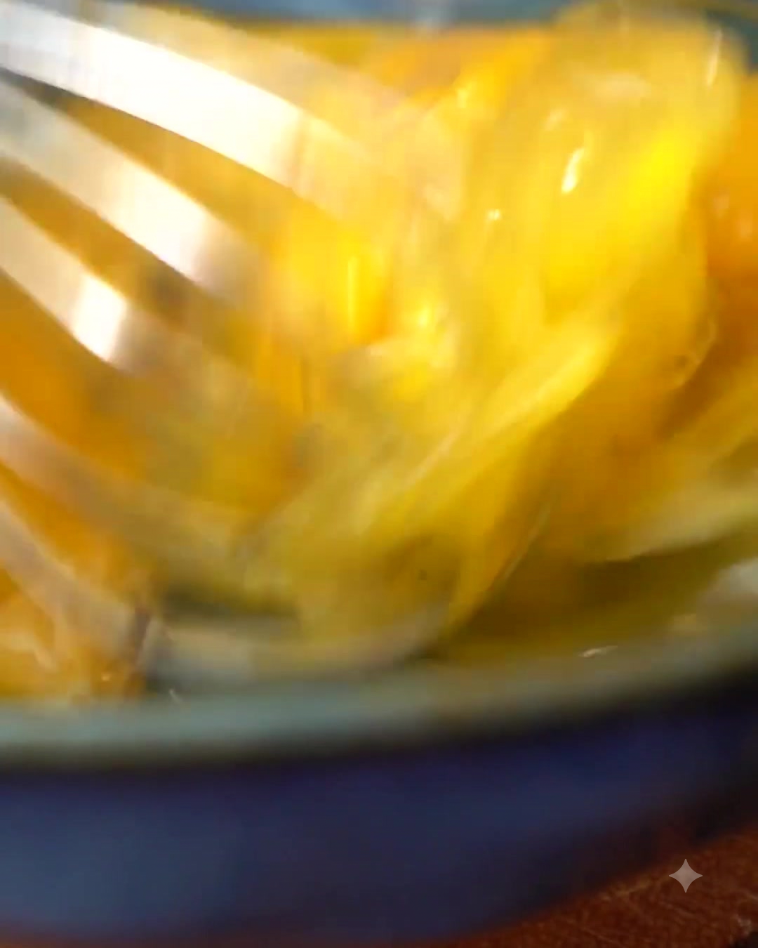 A whisk beating eggs in a bowl with seasonings.