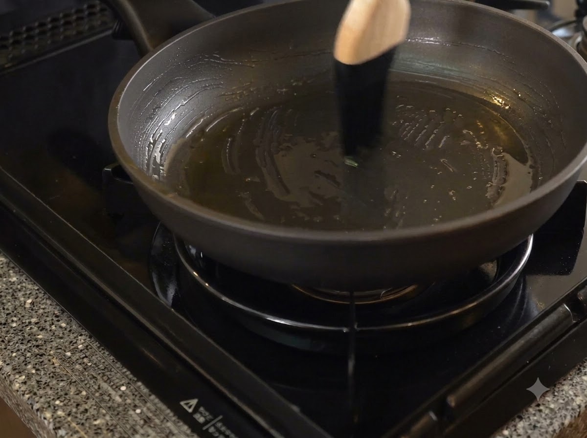 A dark non-stick frying pan being brushed with lard using a wooden-handled basting brush.