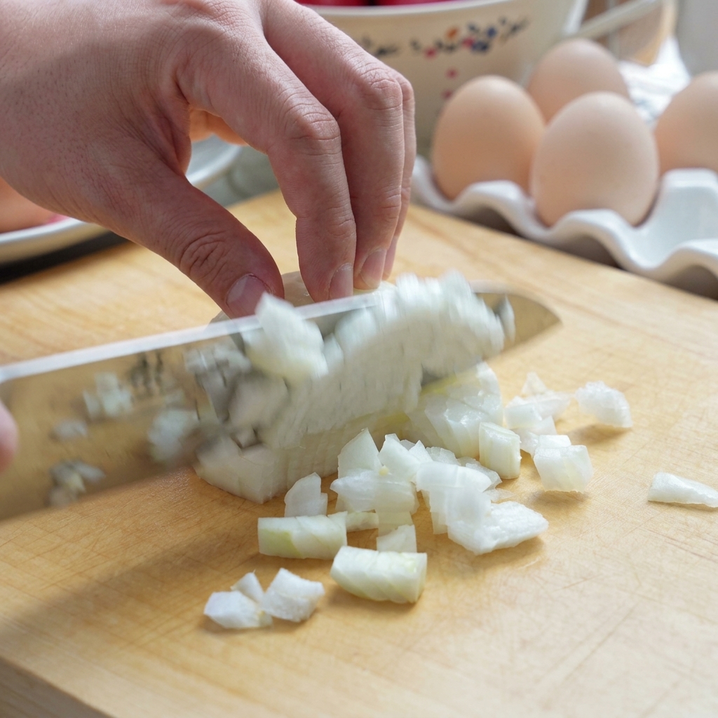 A fresh tomato being chopped into chunks on a wooden cutting board with a knife.