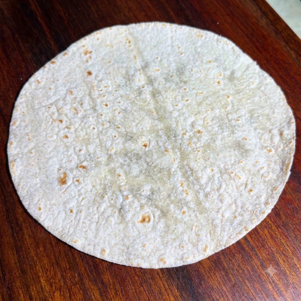 Fresh green lettuce leaves arranged neatly on top of a flat round whole wheat tortilla.