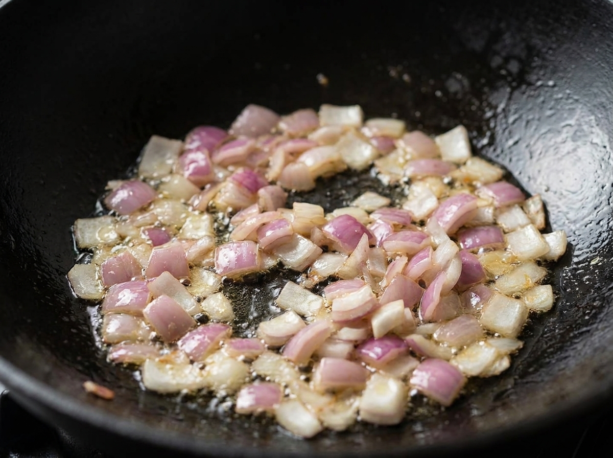 Diced red onions and bacon sizzling and cooking in oil inside a black wok.