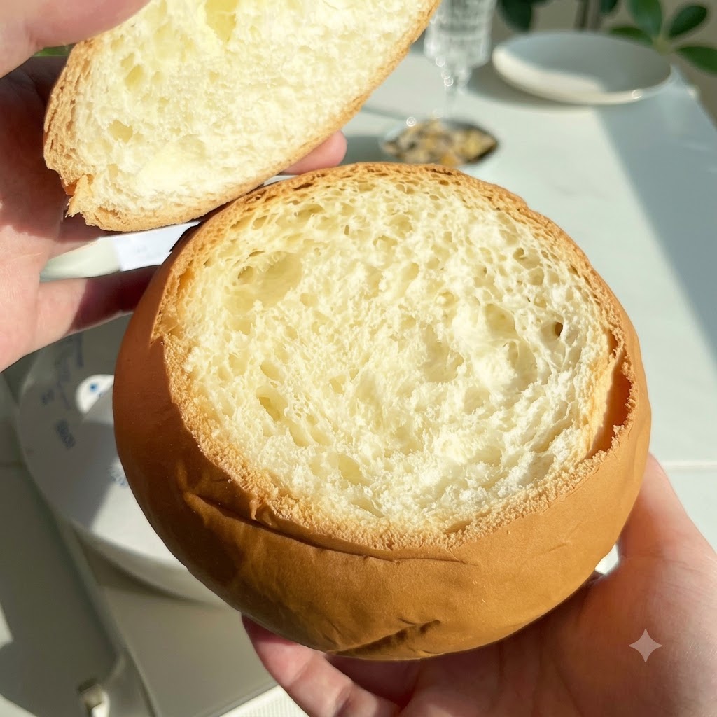A hollowed-out round bread loaf held up with its top lid removed next to it.