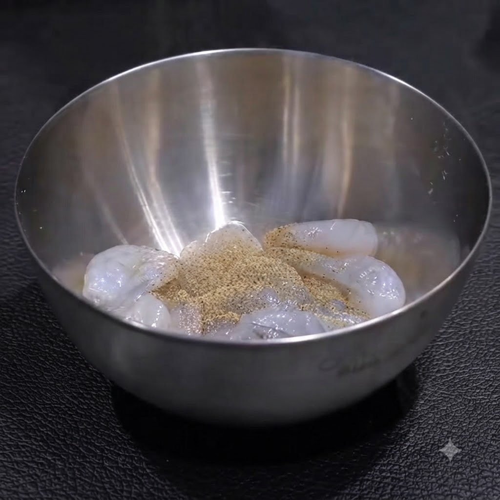 Raw shrimp inside a stainless steel bowl seasoned with a layer of pepper and salt, ready to be mixed.