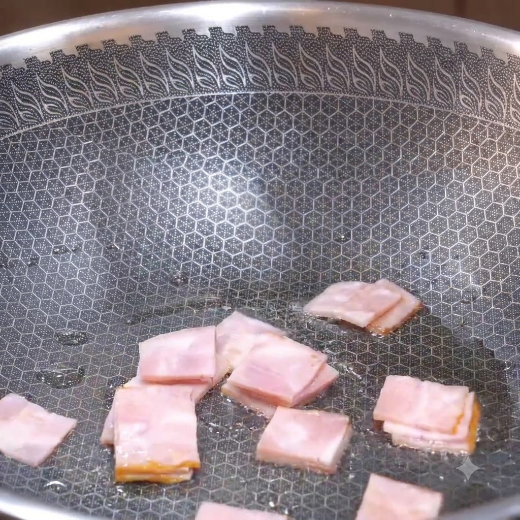Square pieces of bacon being pan-fried in a textured wok until they start to brown.