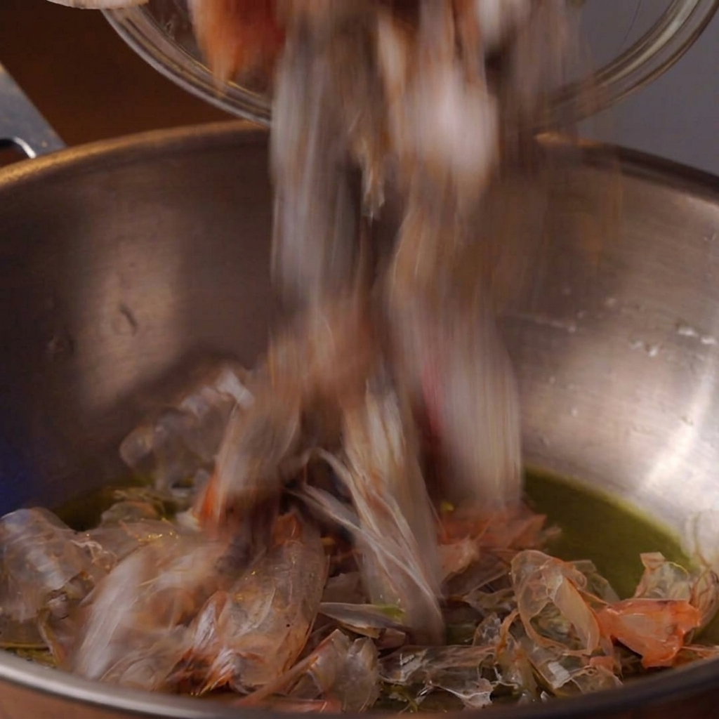 Shrimp heads frying in oil inside a deep metal pot.