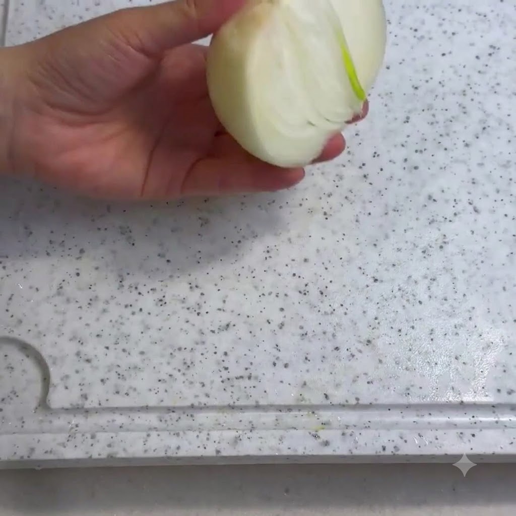 An onion being sliced on a white cutting board with a knife.