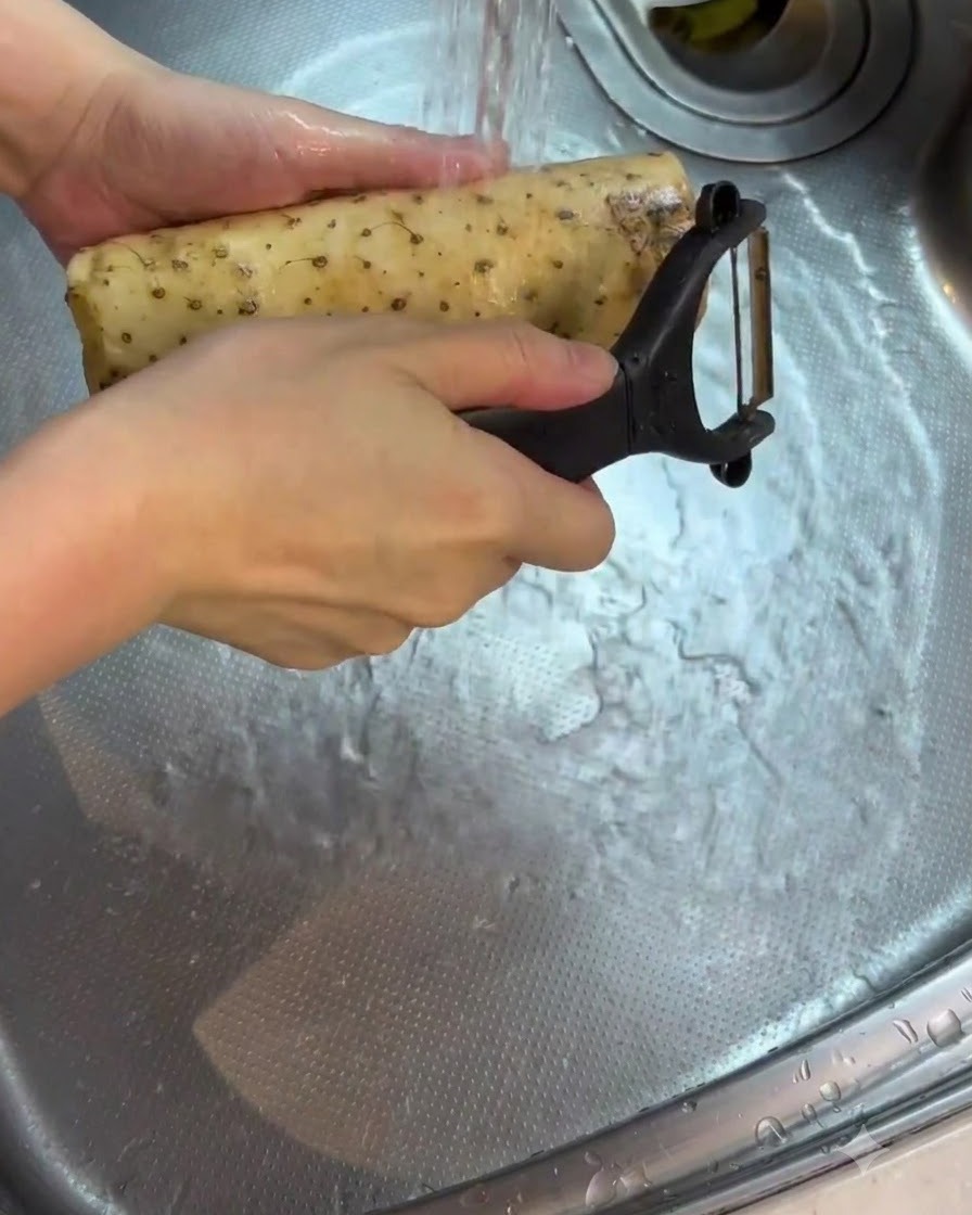A peeled yam being rinsed and cleaned under running water in a sink.