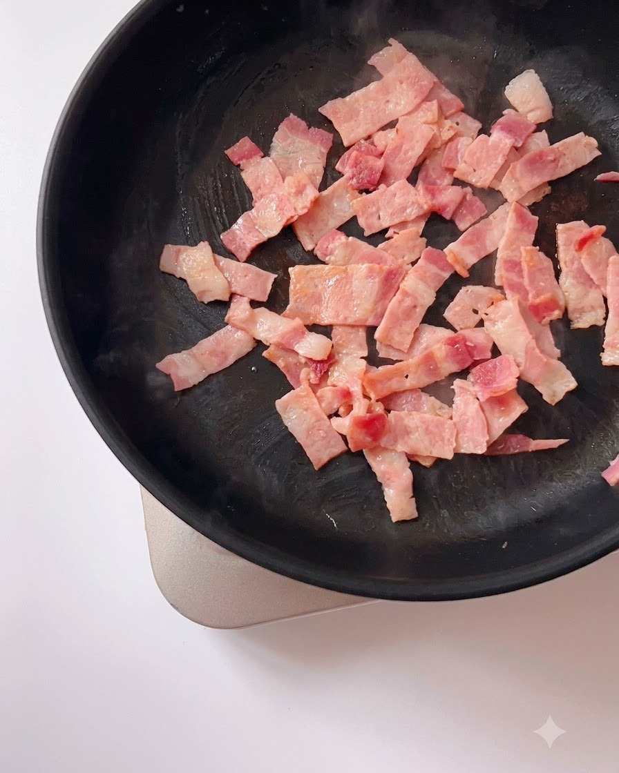 Mashed salted egg yolks mixed with browned bacon pieces sizzling in a frying pan.