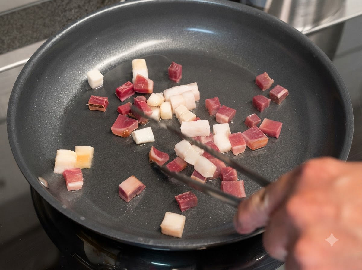 Cubes of bacon and cured meat sizzling in a skillet being turned with metal tongs.