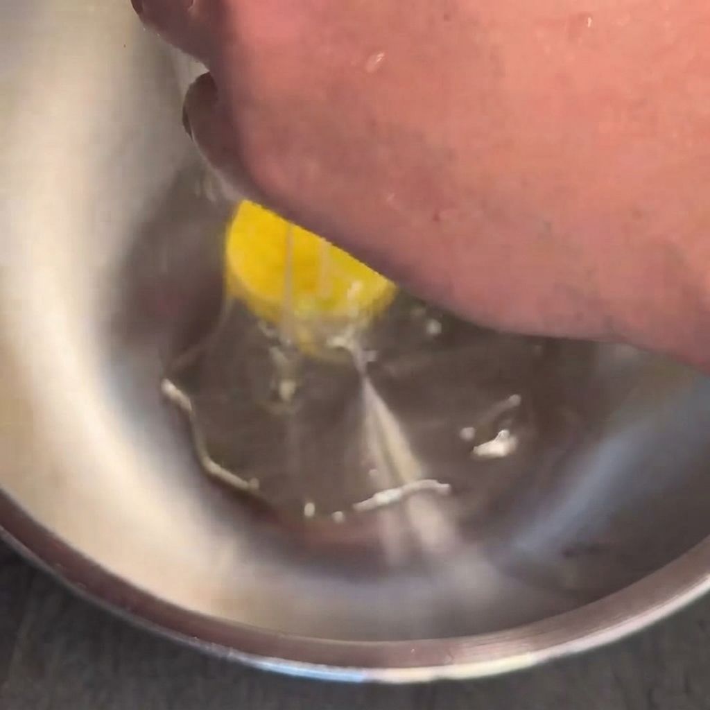An egg being cracked into a stainless steel bowl.