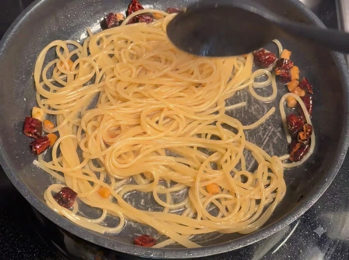 Pasta water being stirred into spaghetti and pork in a skillet.