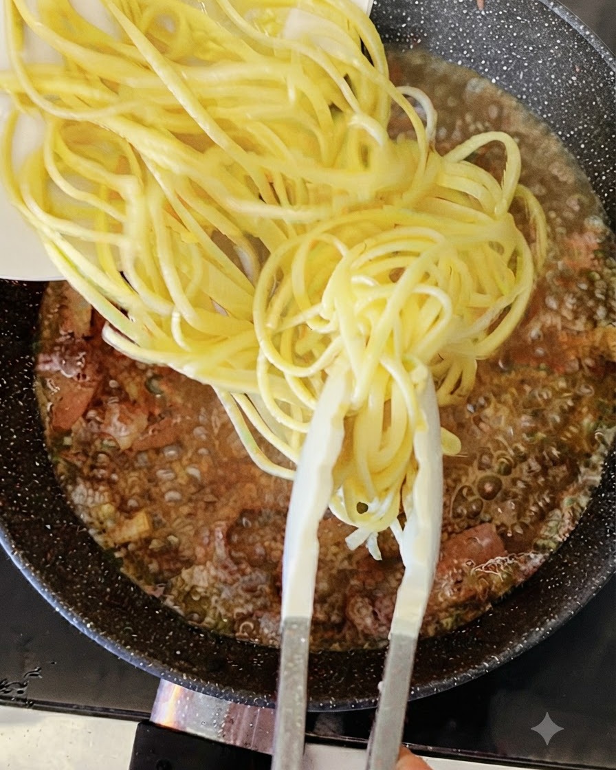 Cooked yellow spaghetti noodles being added with tongs into a bubbling pan of liquid and bacon.