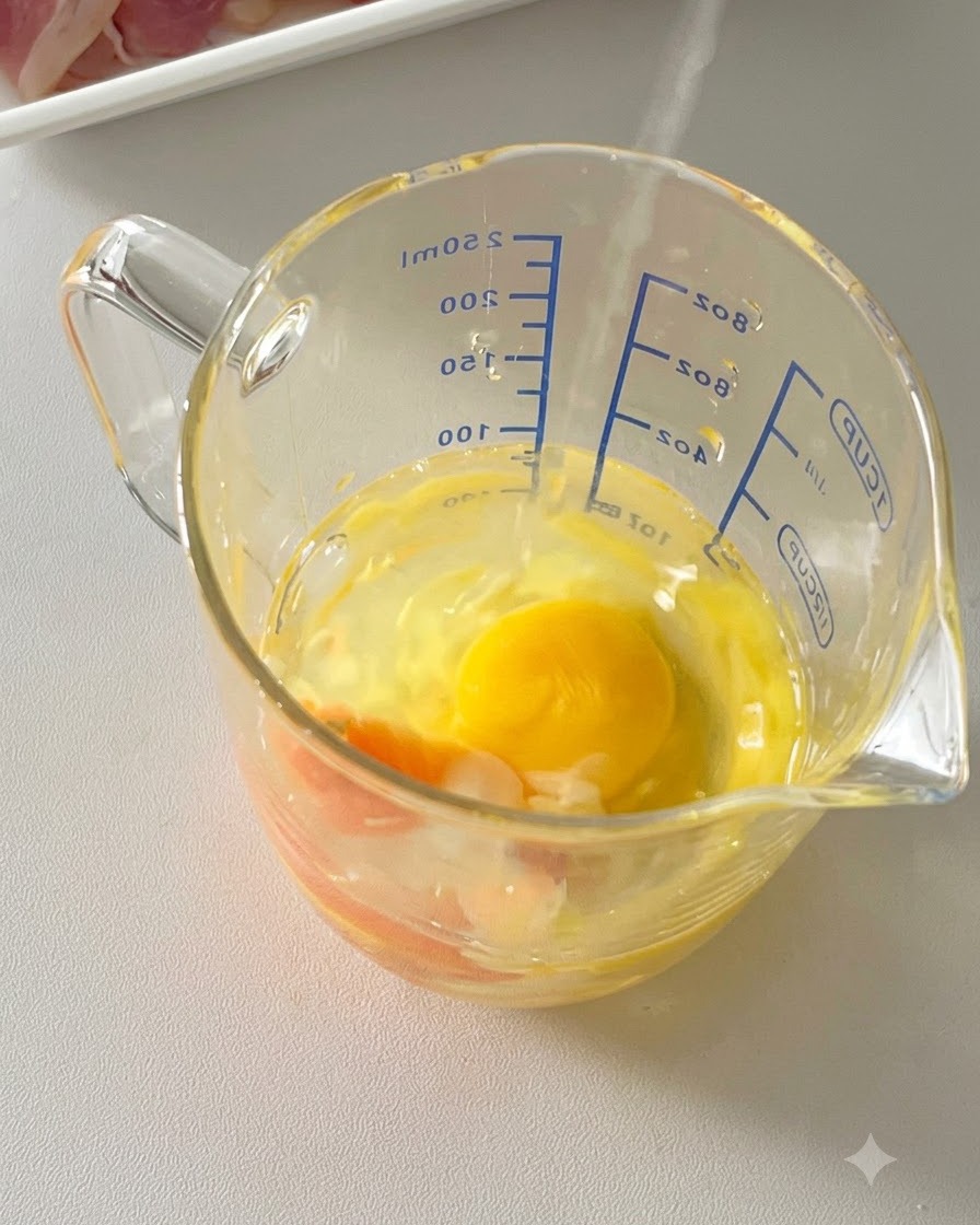 Eggs, grated parmesan cheese, and black pepper combined inside a glass measuring cup.