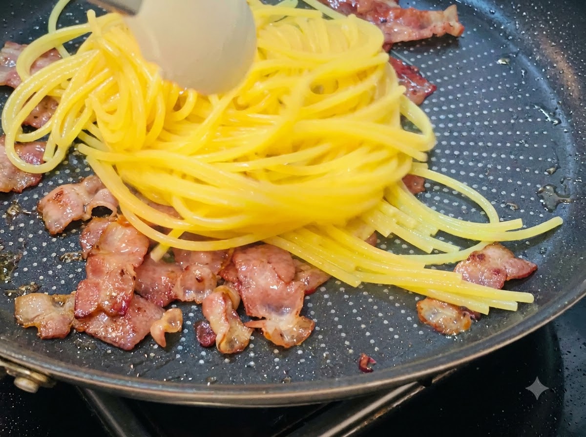 Cooked spaghetti being lifted and transferred into a skillet containing fried bacon pieces.