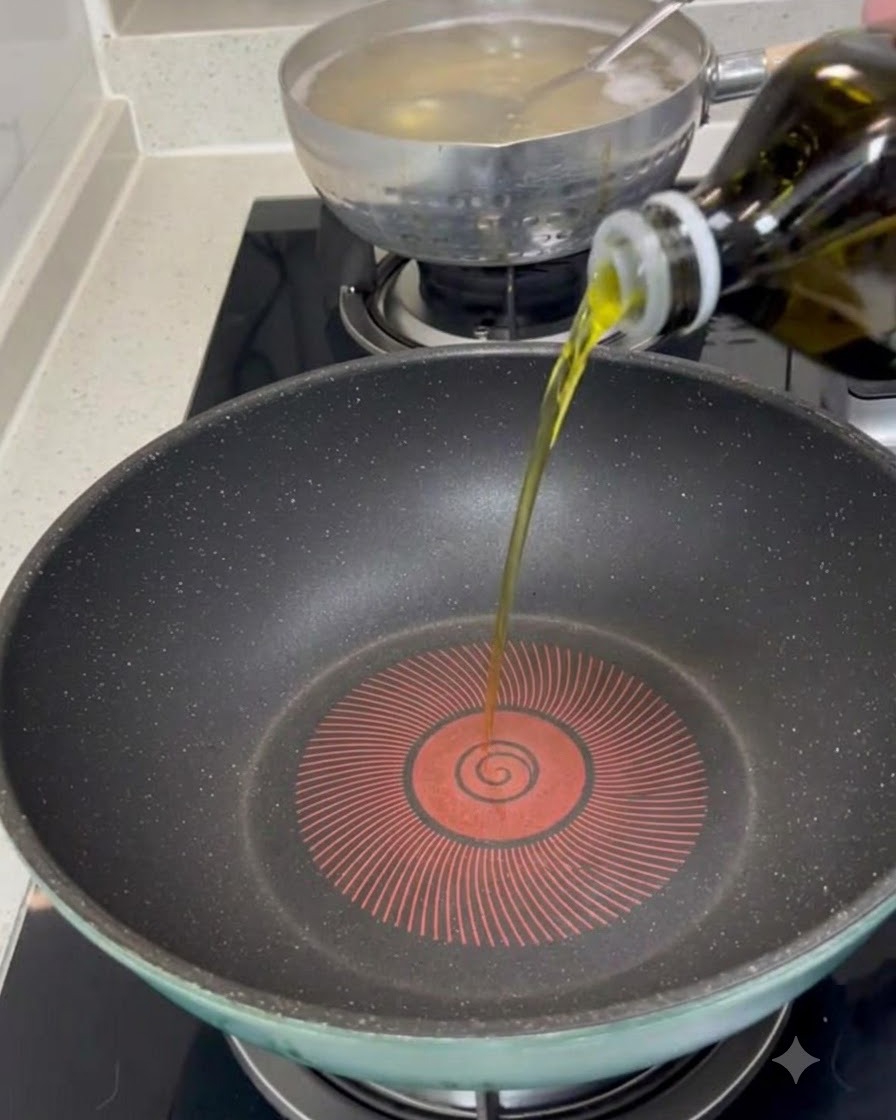 Extra virgin olive oil being poured from a bottle into the center of a preheated dark frying pan.