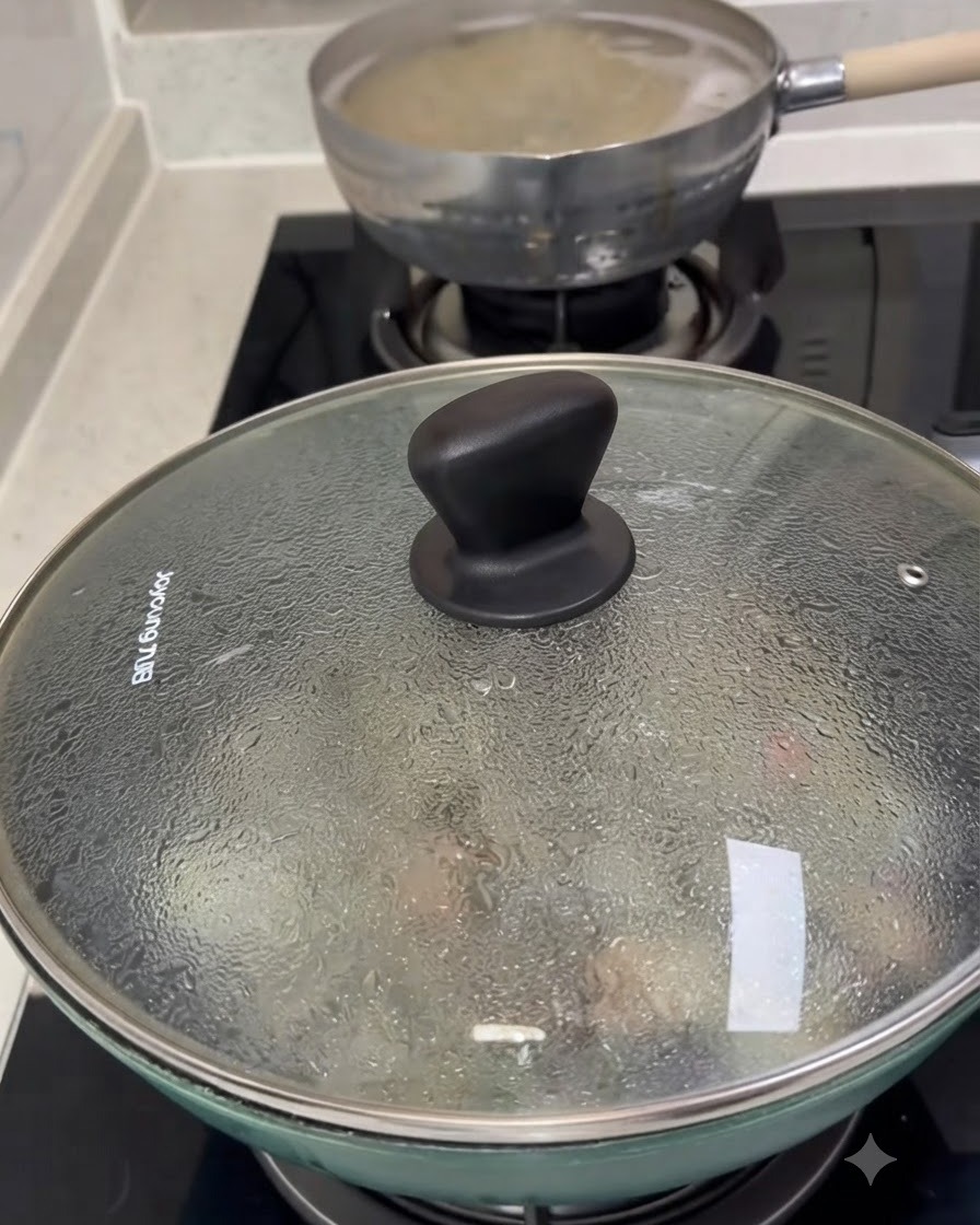 A glass lid covering a pan filled with cooking clams, with condensation visible on the surface.