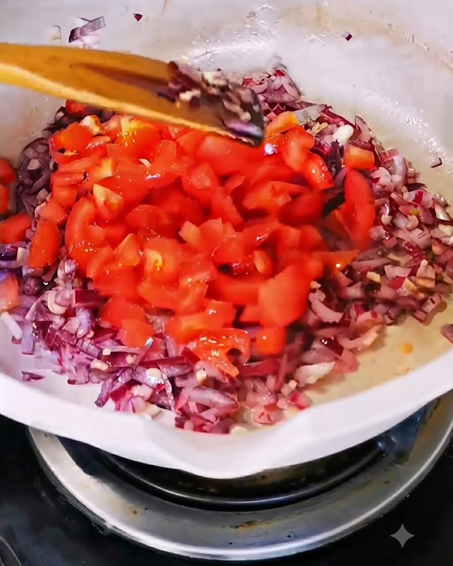 Freshly chopped red tomatoes being added into a white pan containing sautéed onions and garlic.
