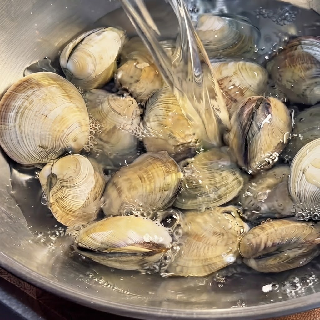 Clams submerged in a bowl of water being thoroughly cleaned by hand.