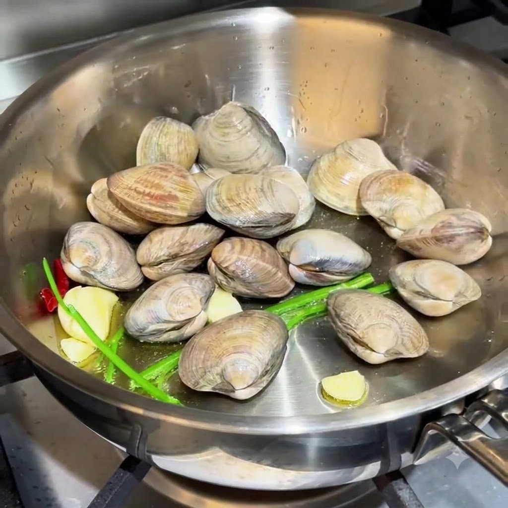 Clams scattered in the pan alongside garlic and chive roots.