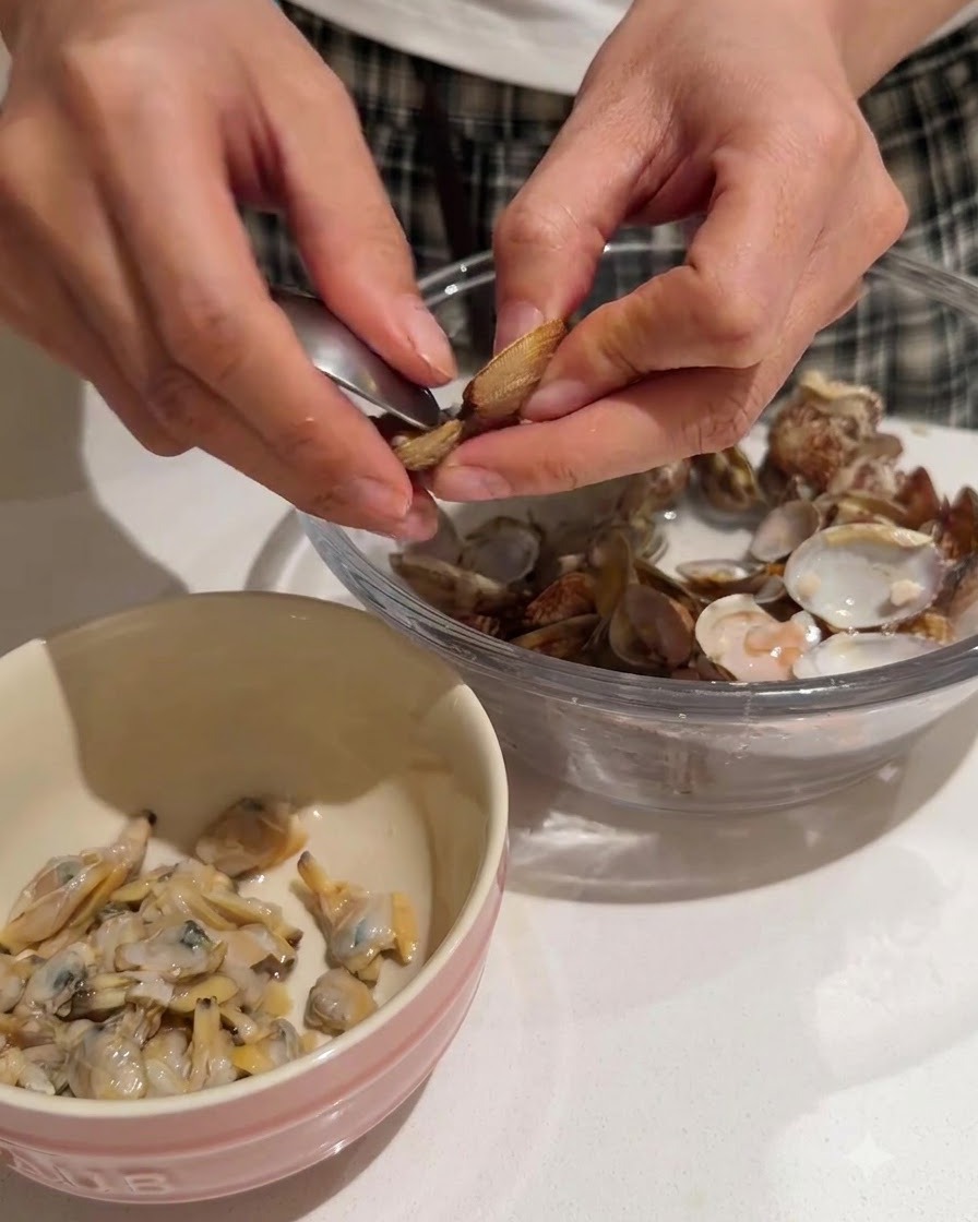 Hands extracting tender clam meat from shells into a pink-rimmed bowl.