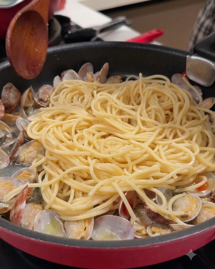 A wooden spoon and spaghetti pasta in a pan with open clams and broth.